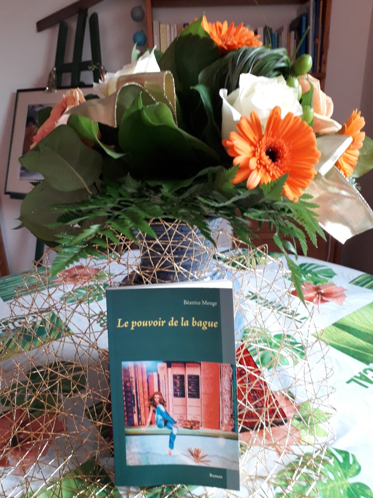 Le roman Le pouvoir de la bague posé sur une table avec un bouquet de fleurs.